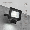 Black outdoor LED floodlight with a built-in motion sensor, mounted on a gray concrete wall. The image includes text and icons indicating weather resistance and suitability for sunny, snowy, foggy, and rainy conditions.