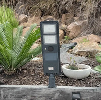 A solar sensor floodlight illuminated against a backdrop of lush greenery.