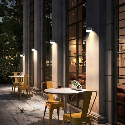 Outdoor patio area with yellow furniture and a round table, illuminated by wall-mounted sensor solar lights attached to gray columns.