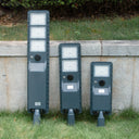 Three solar-powered street lights against a stone wall with grass in the foreground